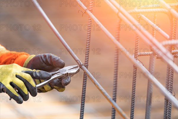 Worker securing steel rebar framing with wire plier cutter tool at construction site