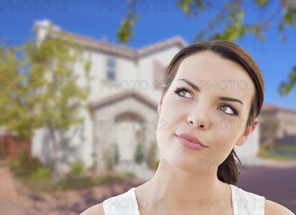 Thoughtful pretty mixed-race woman in front of house looking up and to the side