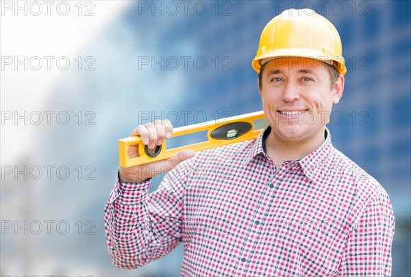 Young male contractor with hard hat and level in front of building