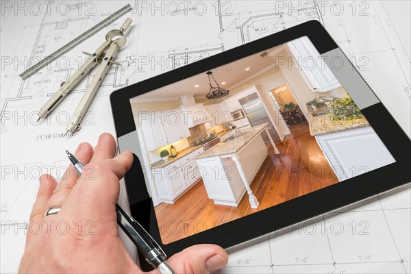 Hand of architect on computer tablet showing custom kitchen photo over house plans