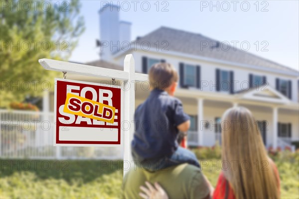 Curious family facing sold for sale real estate sign and beautiful new house