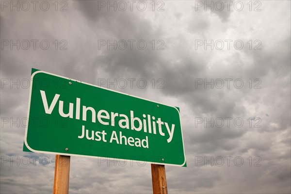 Vulnerability just ahead green road sign with dramatic storm clouds and sky