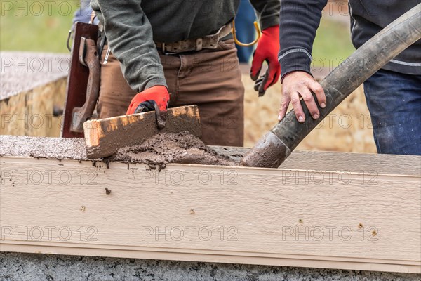 Construction workers pouring and leveling wet cement into wood framing