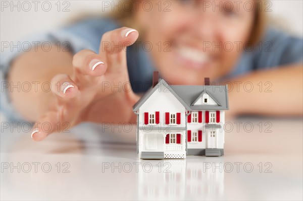 Smiling woman reaching for model house on a white surface