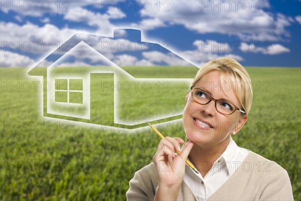 Contemplative woman in grass field looking up and over to the side with ghosted house figure behind