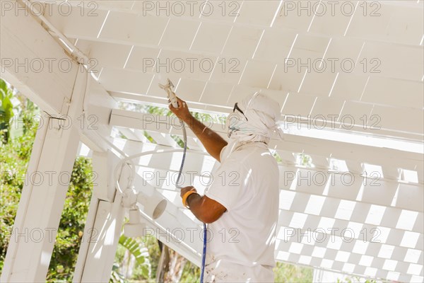 House painter wearing facial protection spray painting A deck of A home