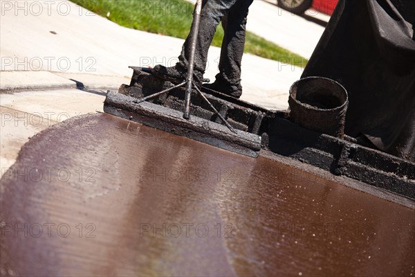 Road worker resurfacing street with hot tar