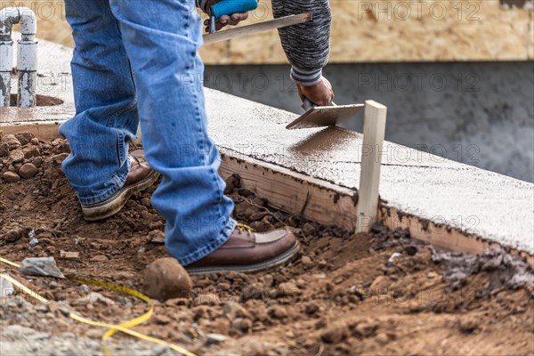 Construction worker using wood trowel on wet cement forming coping around new pool