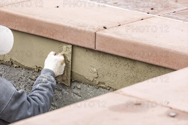 Tile worker applying cement with trowel at pool construction site