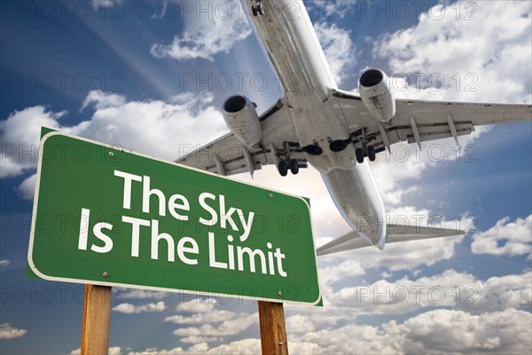 The sky is the limit green road sign and airplane above with dramatic blue sky and clouds