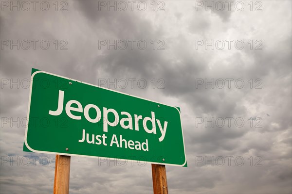 Jeopardy just ahead green road sign with dramatic storm clouds and sky