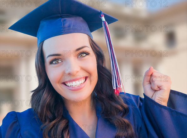 Happy graduating mixed-race woman in cap and gown celebrating on campus