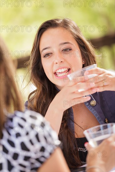 Expressive young adult woman having drinks and talking with her friend outdoors