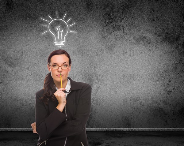 Light bulb drawn above head of young adult woman with pencil in front of wall with copy space