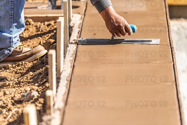 Construction worker using trowel on wet cement forming coping around new pool