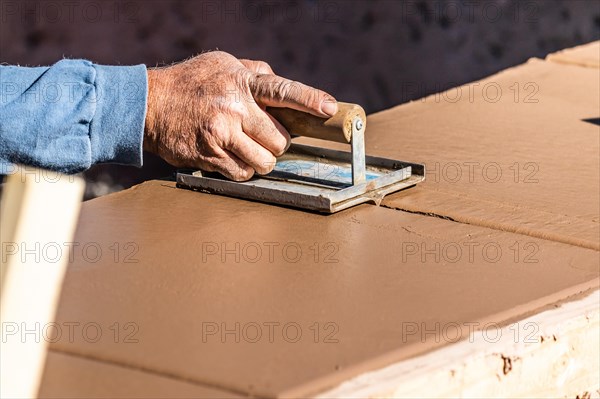 Construction worker using hand groover on wet cement forming coping around new pool