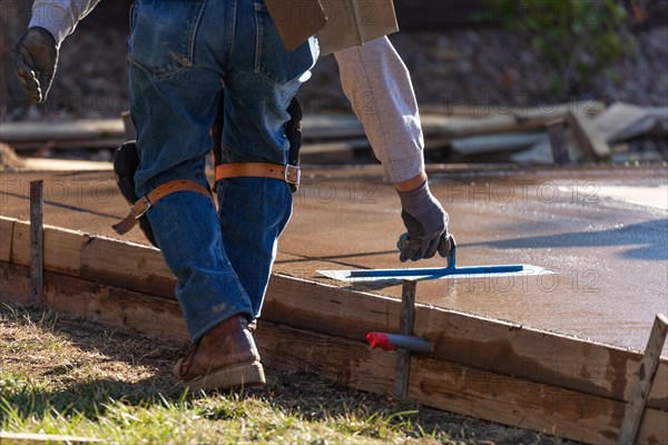 Construction worker smoothing wet cement with trowel tools