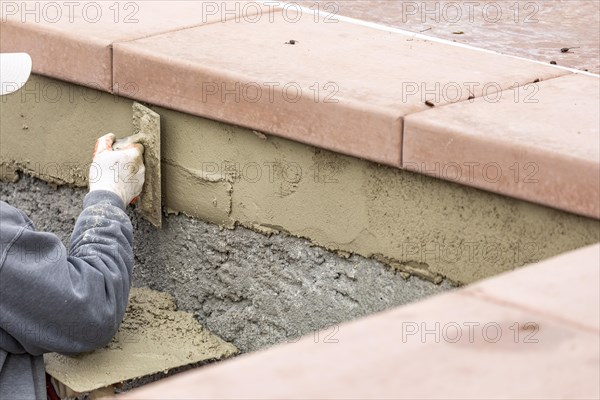 Tile worker applying cement with trowel at pool construction site