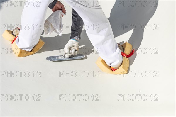 Worker wearing sponges on shoes smoothing wet pool plaster with trowel