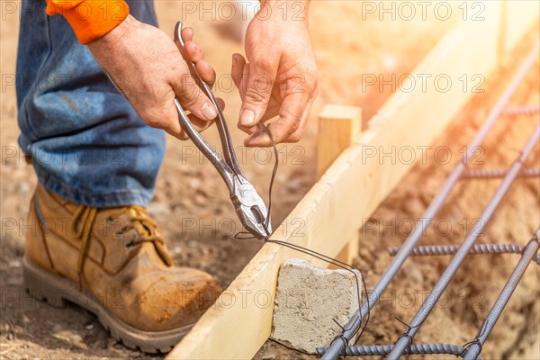 Worker securing steel rebar framing with wire plier cutter tool at construction site