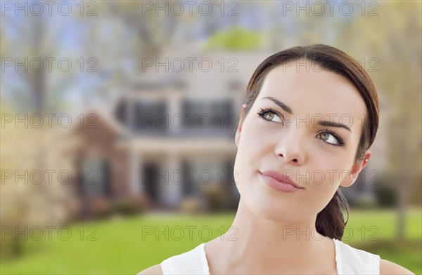 Thoughtful pretty mixed-race woman in front of house looking up and to the side