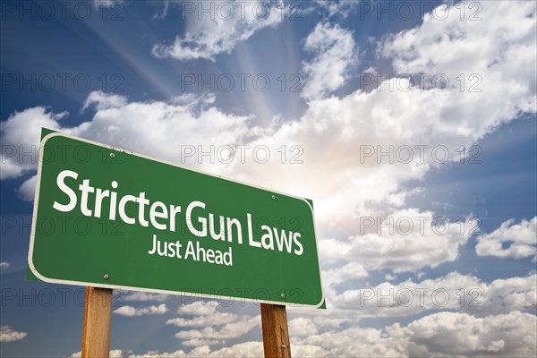 Stricter gun laws green road sign with dramatic clouds and sky