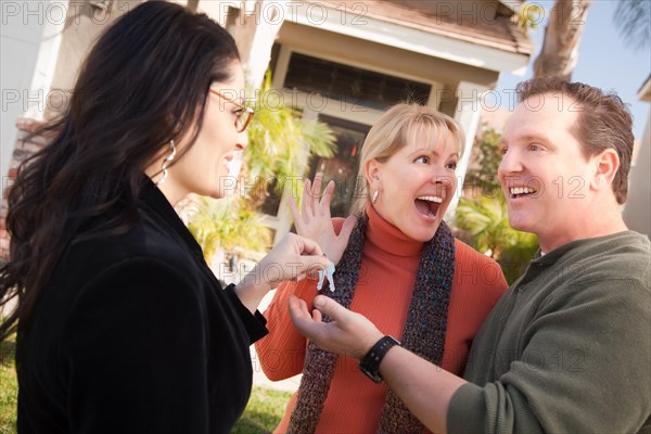 Hispanic female real estate agent handing over new house keys to excited couple