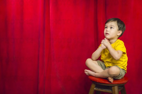 Handsome mixed-race boy sitting on stool in front of red curtain