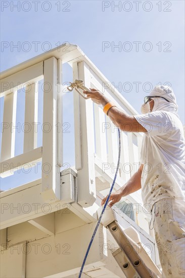 House painter wearing facial protection spray painting A deck of A home