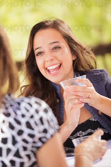 Expressive young adult woman having drinks and talking with her friend outdoors