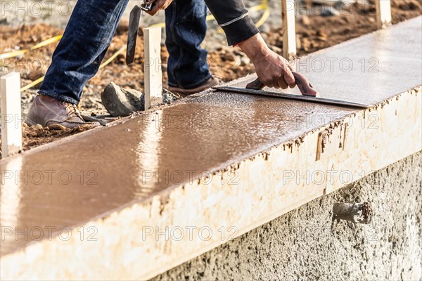 Construction worker using wood trowel on wet cement forming coping around new pool