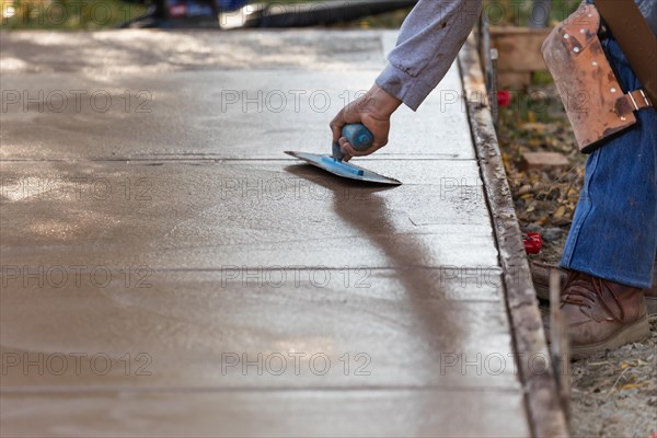 Construction worker smoothing wet cement with trowel tools