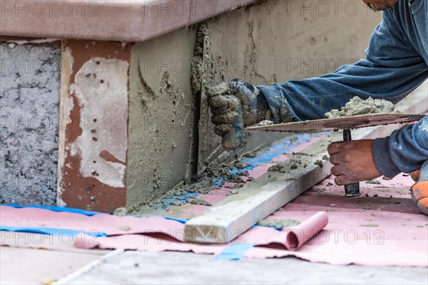 Tile worker applying cement with trowel at pool construction site