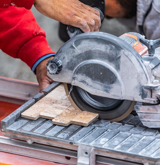 Worker using wet tile saw to cut wall tile at construction site