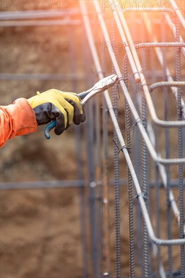 Worker securing steel rebar framing with wire plier cutter tool at construction site