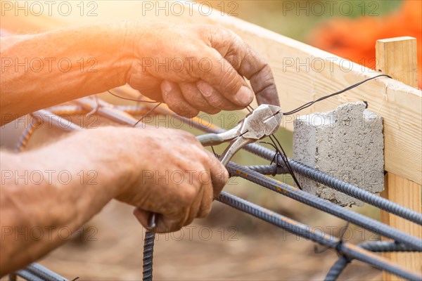 Worker securing steel rebar framing with wire plier cutter tool at construction site