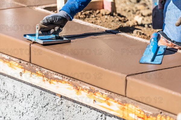 Construction worker using hand groover on wet cement forming coping around new pool