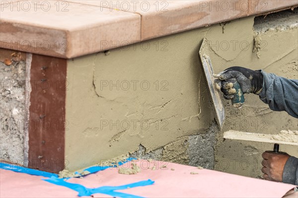 Tile worker applying cement with trowel at pool construction site