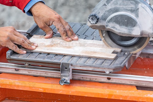 Worker using wet tile saw to cut wall tile at construction site