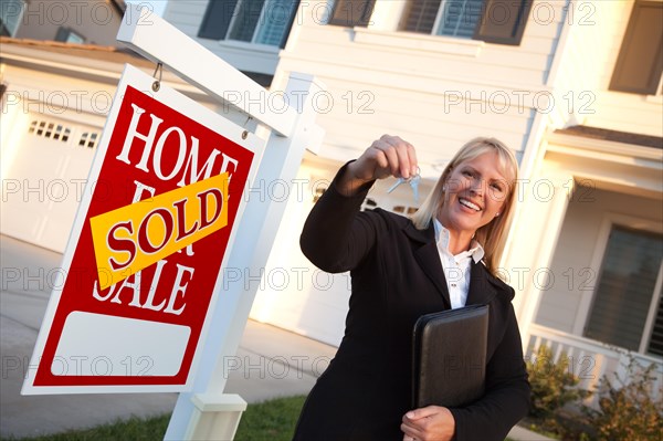 Female real estate agent handing over the house keys in front of a beautiful new home and real estate sign