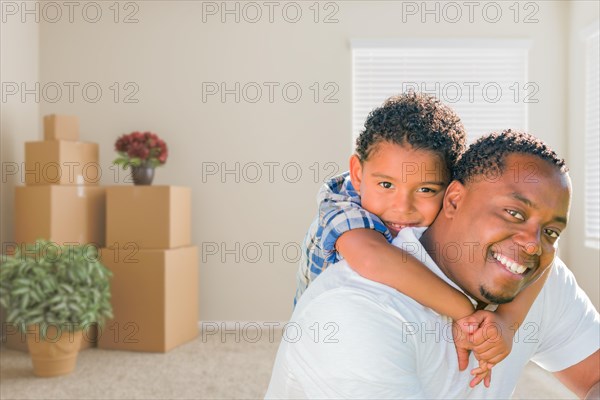 Happy mixed-race african american father and son in room with packed moving boxes