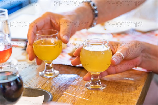 Man and woman picking up small glass of micro brew beer at bar