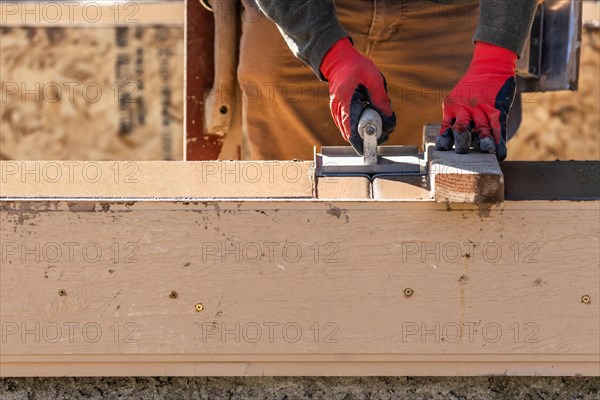 Construction worker using hand groover on wet cement forming coping around new pool