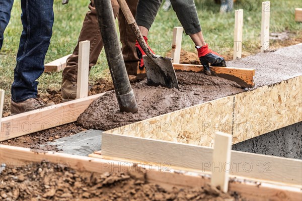 Construction workers pouring and leveling wet cement into wood framing