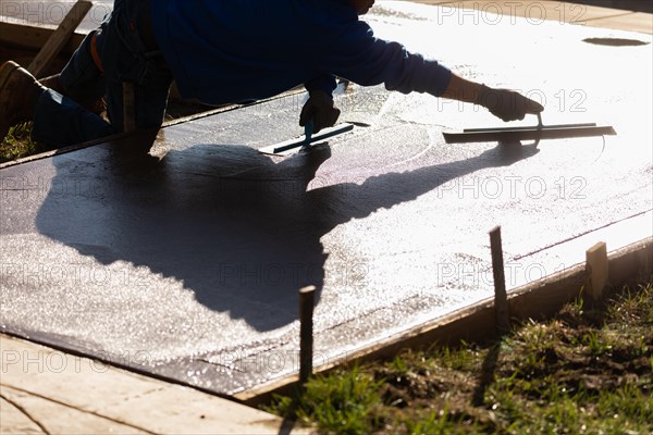 Construction worker smoothing wet cement with trowel tools