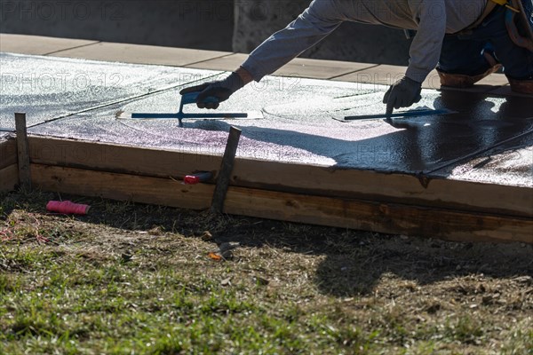 Construction worker smoothing wet cement with trowel tools