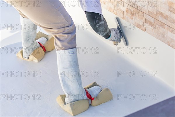 Worker wearing sponges on shoes smoothing wet pool plaster with trowel