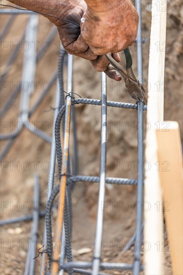 Worker securing steel rebar framing with wire plier cutter tool at construction site