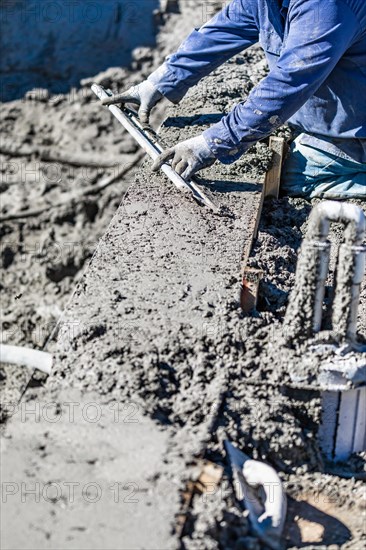 Pool construction worker working with A smoother rod on wet concrete