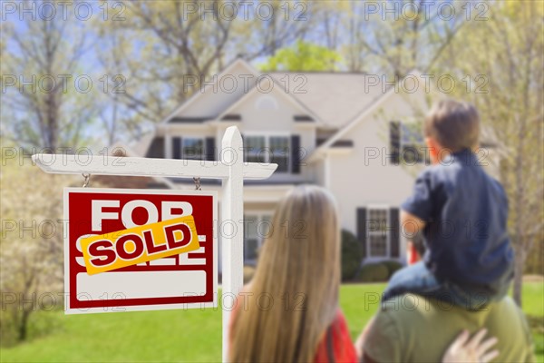 Curious family facing sold for sale real estate sign and beautiful new house